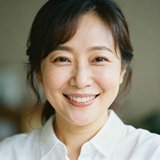 一位笑容温暖的年轻妈妈，穿着简约的白色衬衫，在自然光下呈现出亲切柔和的气质。