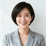 一位短发干练的职场女性正面微笑，穿着浅灰色西装外套，展现出自信与温和并存的气质，背景为简约白墙。
